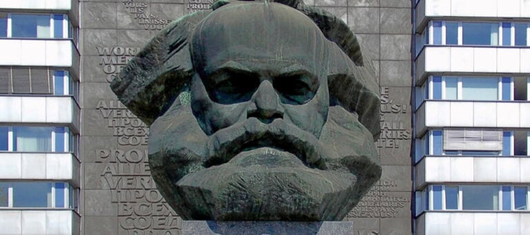 Monumental bust of Karl Marx, with multilingual text on surrounding wall.
