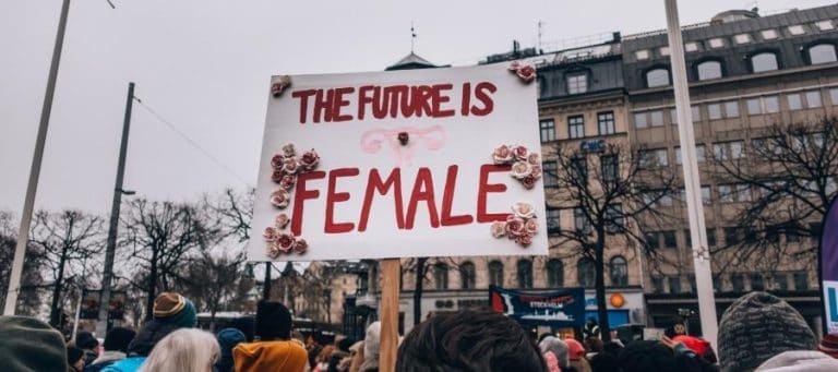 Protest sign reading "The future is female" with uterus symbol and flowers.
