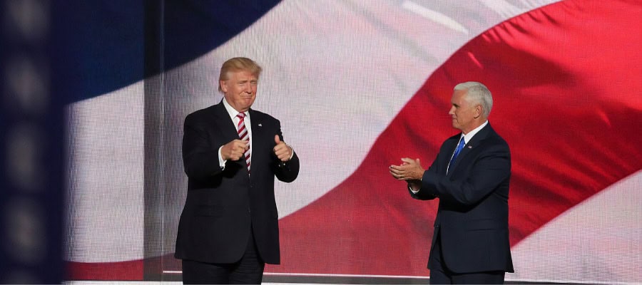 Donald Trump and Mike Pence at a political event, giving thumbs up and applauding.