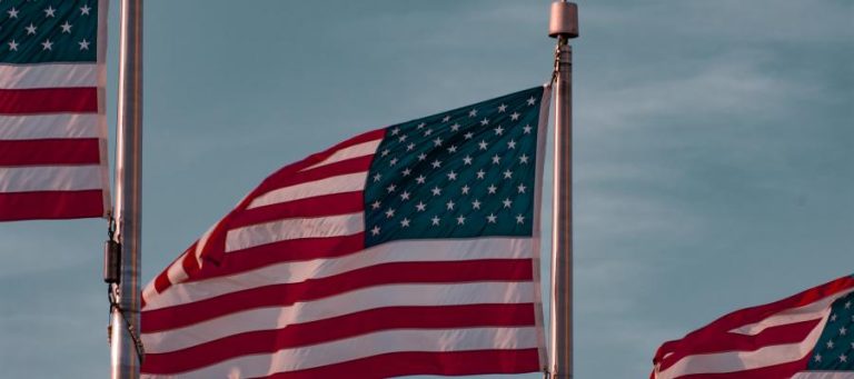 American flags waving in the wind against a blue sky.