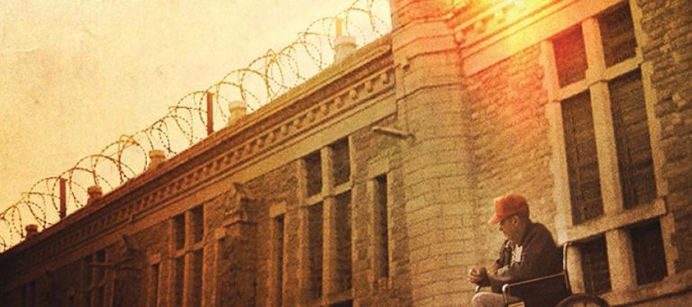 Man in wheelchair outside prison, contemplating existence.