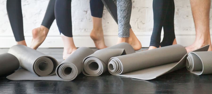 Rolled-up yoga mats on a dark floor, with bare feet of several people visible.
