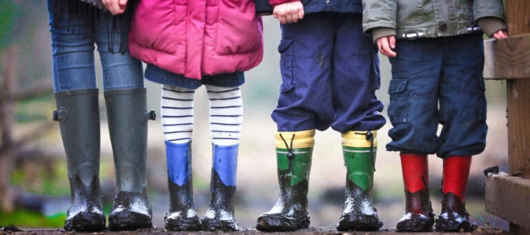 Four children in muddy rain boots stand together, showcasing a sense of community and childhood exploration.