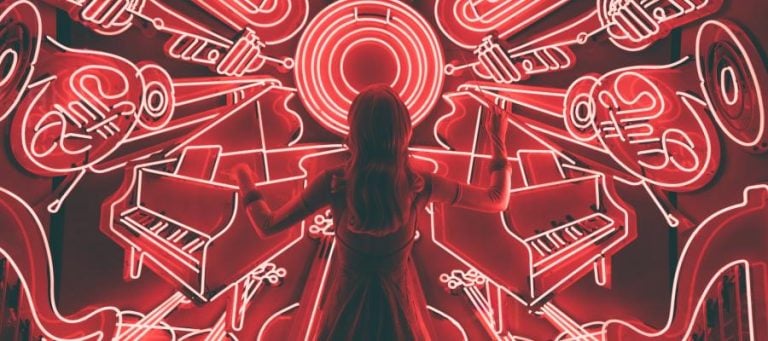 Woman standing before a neon-lit wall depicting musical instruments, including pianos and brass instruments.