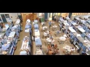 Overcrowded prison dormitory with inmates on cots, illustrating the harsh realities of incarceration and lack of dignity.