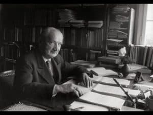 Martin Heidegger, renowned philosopher, sits at his desk surrounded by books and papers.