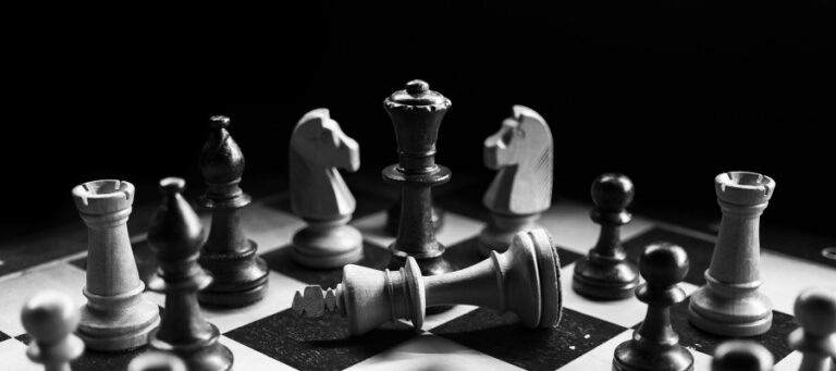 Black and white chess pieces on a board, with the white king knocked down.
