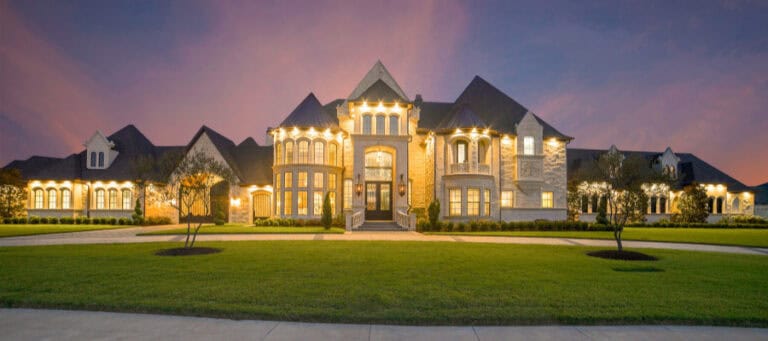 Luxury mansion at dusk, illuminated exterior.