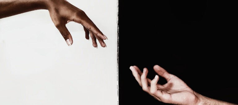 Two hands reaching across a black and white divide.