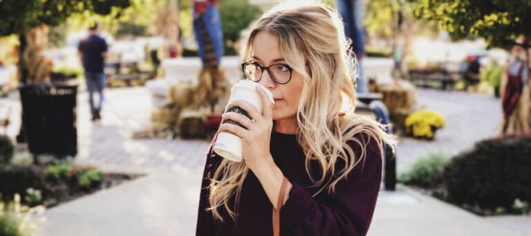Young woman with blonde hair enjoys a coffee outdoors.