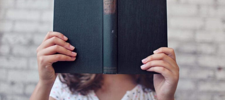 Woman's face hidden behind a book titled "Winter Comes."