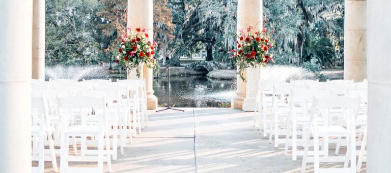 White chairs arranged for an outdoor wedding ceremony near a pond.