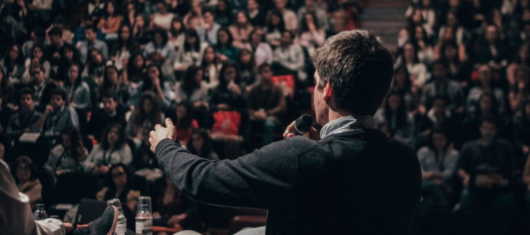 Speaker addressing a large audience, holding a microphone.