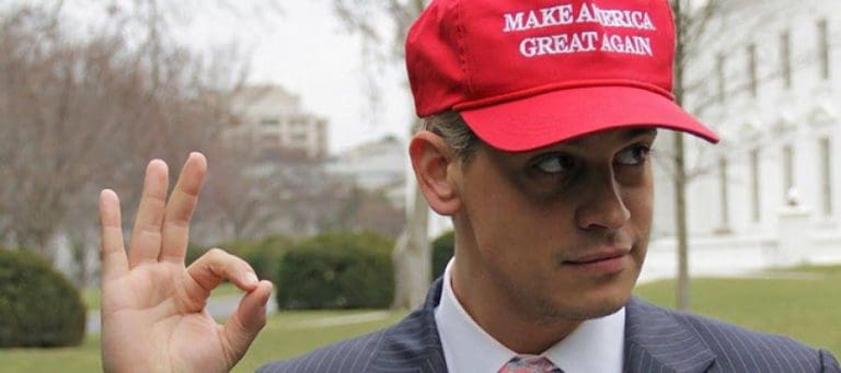 Man in suit and "Make America Great Again" hat makes OK gesture.