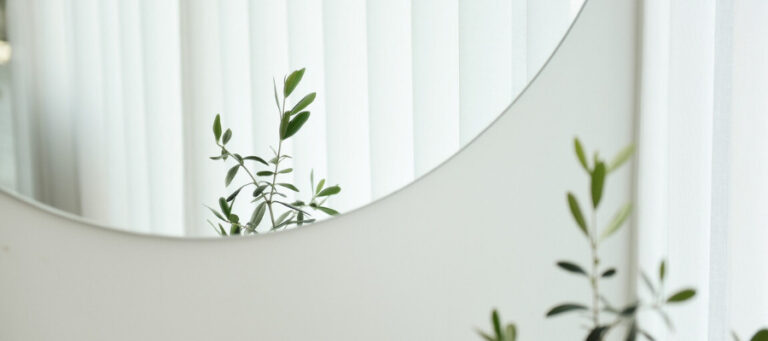 A half-round mirror reflects a plant and sheer curtains.