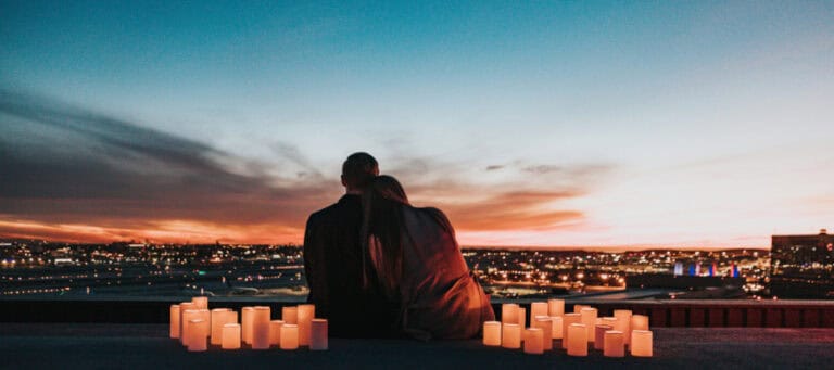 Couple embracing on rooftop at sunset, overlooking city lights.