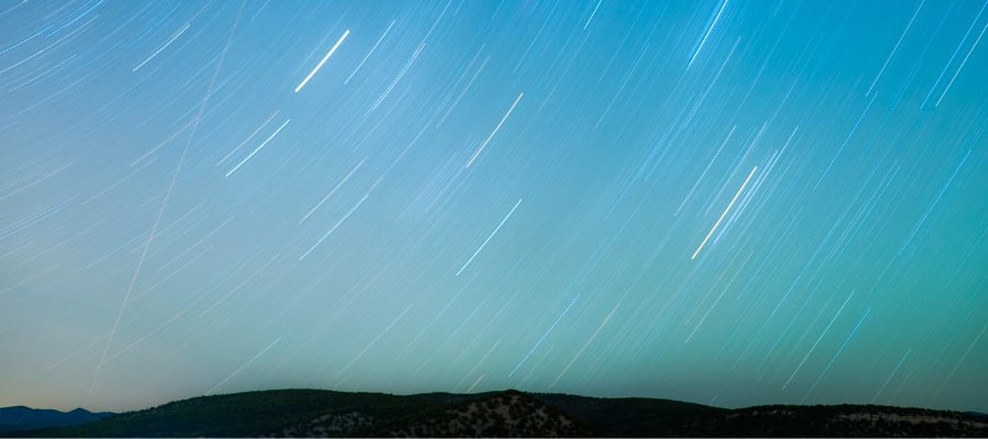 Star trails over a dark mountain range at night.