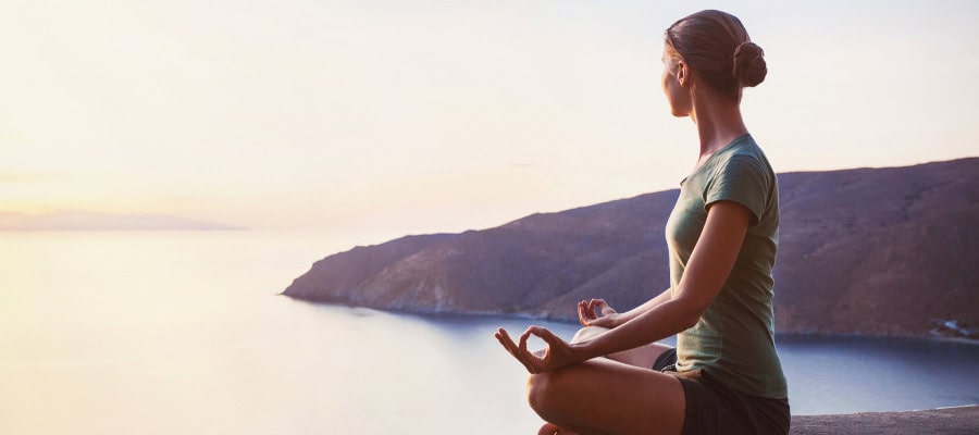 Woman meditating on a cliff overlooking the ocean at sunset.