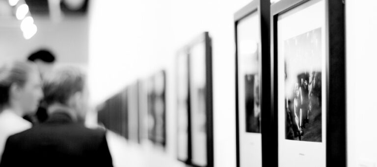 Black and white photographs displayed in an art gallery. People view the artwork.