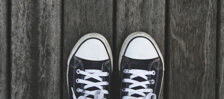 A pair of worn black canvas sneakers on a wooden surface.