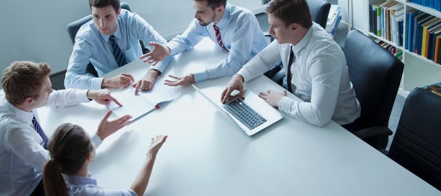 Business team collaborating around a table, discussing documents and using a laptop.