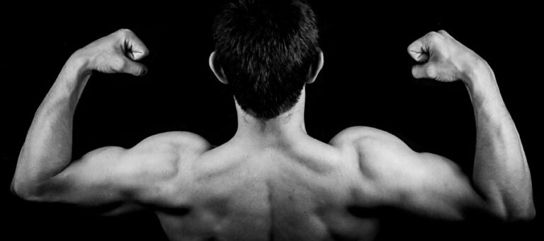 Man flexing biceps, back view. Muscular physique.