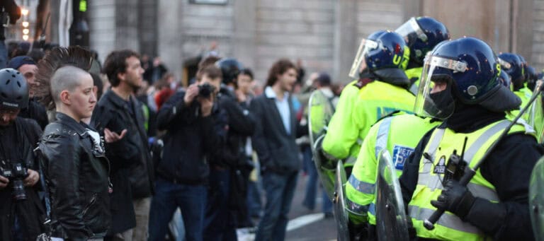 Police officers in riot gear face a crowd of protestors.