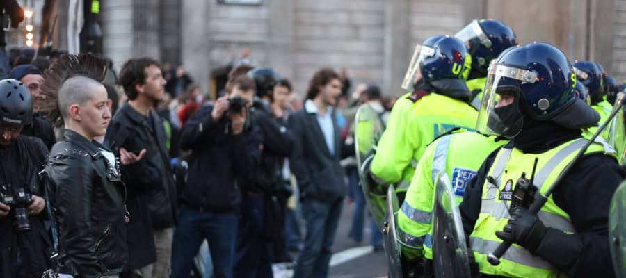 Police officers in riot gear face a crowd of protestors.