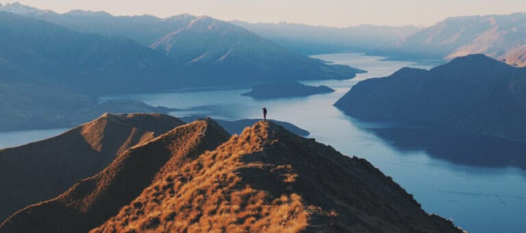 Person standing on mountain overlooking a lake and valley.