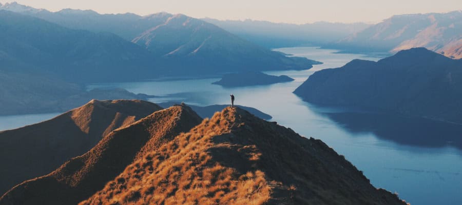 Person standing on mountain overlooking a lake and valley.