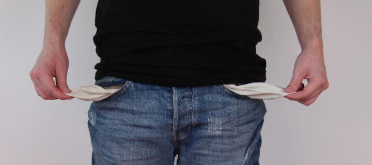 Person showing empty pockets, illustrating financial hardship.