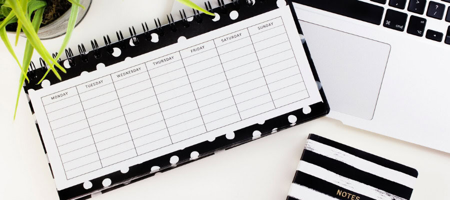 Weekly planner with days of the week labeled, open laptop, and small notebook.