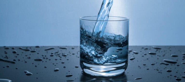 Glass of water being filled, water droplets on a dark surface.