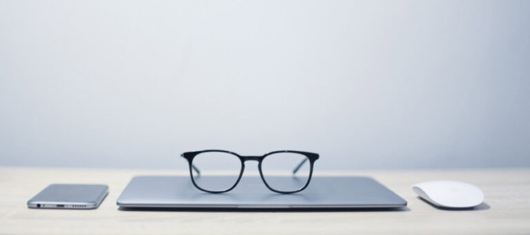 Laptop, eyeglasses, and wireless mouse on a desk.