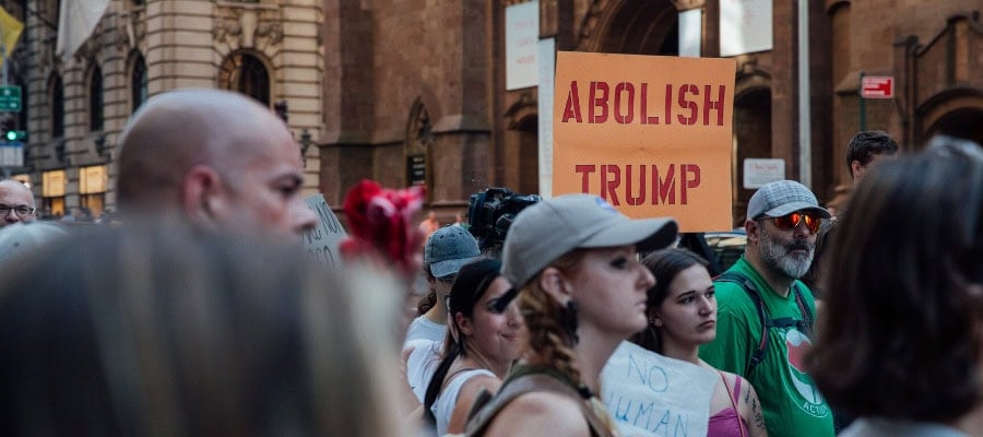 Protestors holding signs reading "Abolish Trump" at a demonstration.