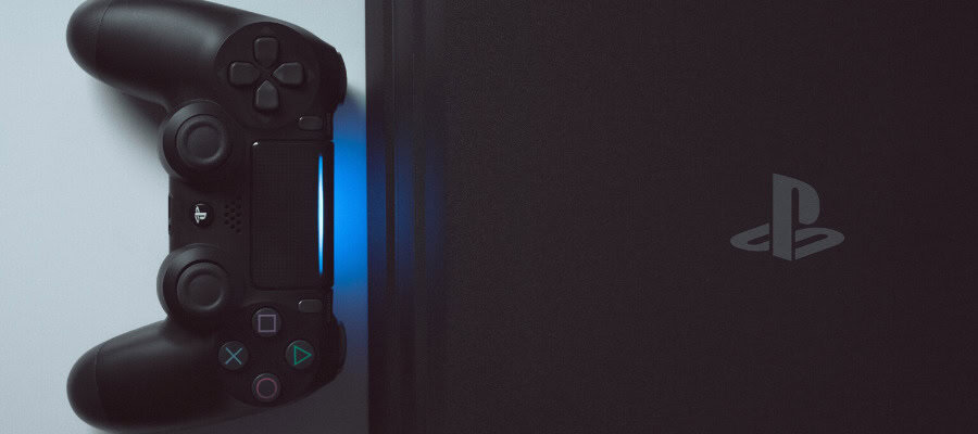 Black PlayStation 4 console with controller. The controller has a blue light.