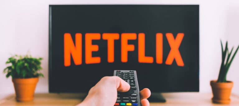 Hand holding Netflix remote, Netflix logo on TV screen