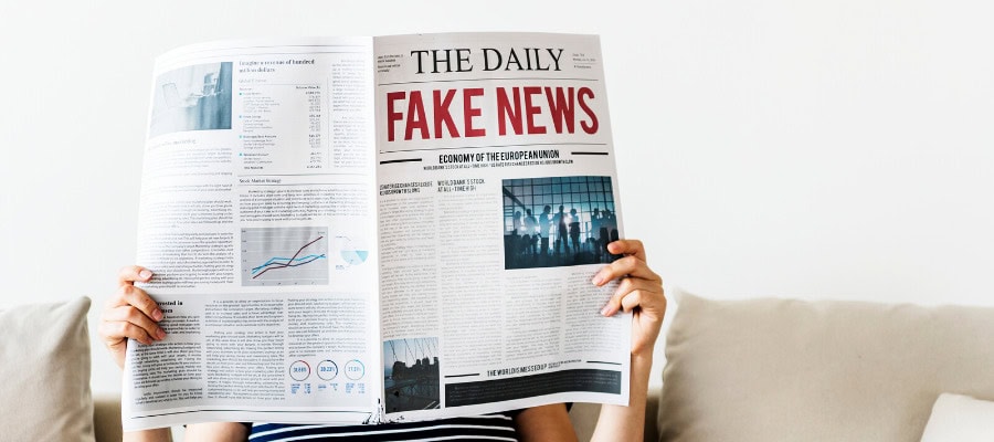 Person reading a newspaper headline that says "Fake News.
