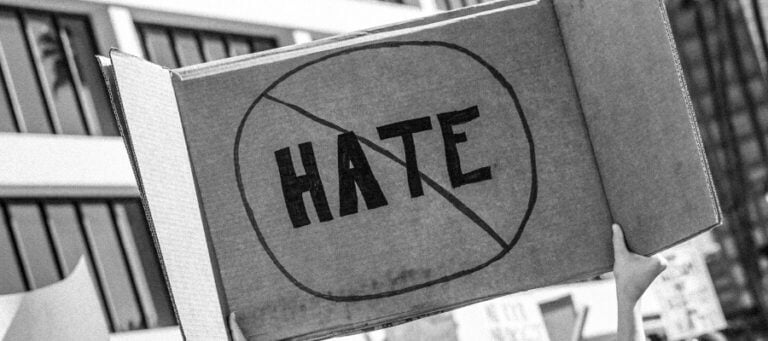 Cardboard sign with a red circle and slash over the word "HATE," symbolizing anti-hate.