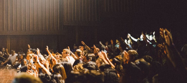 Diverse crowd of people with raised hands at a conference or event.