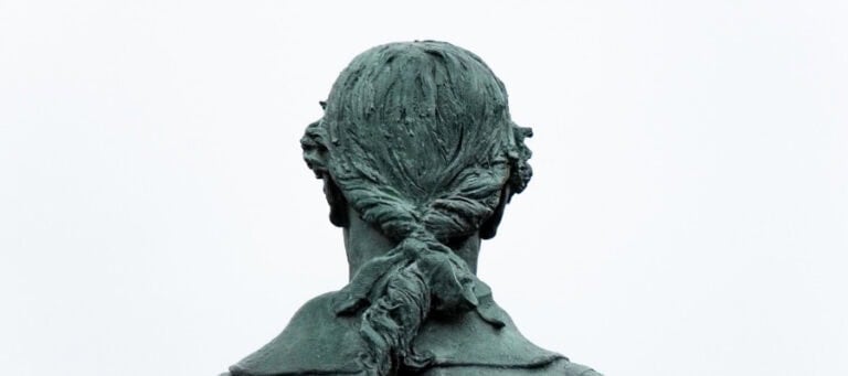 Rear view of a bronze statue, hair styled in a ponytail.