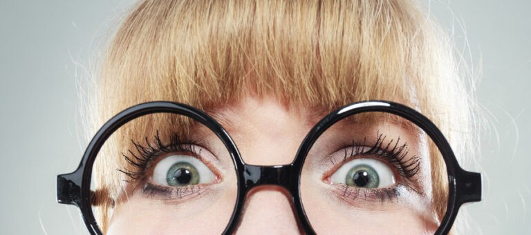Close-up of wide-eyed woman wearing round glasses.