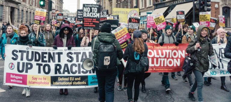 Protestors march against racism, holding signs that read "No to Racism" and "Refugees Welcome.