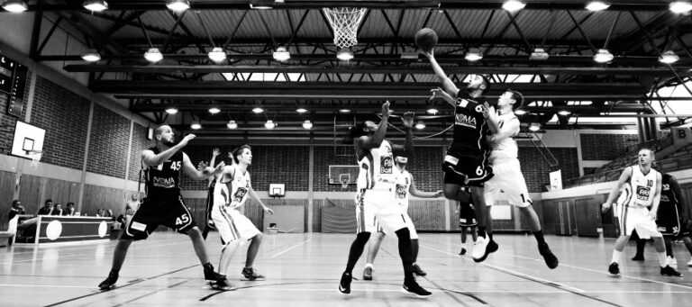 Black and white photo of a basketball game in progress. Players are jumping and shooting.