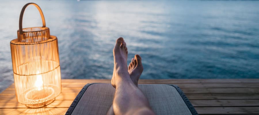 Person's feet up, relaxing by the water at sunset.
