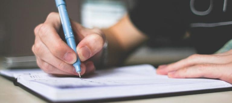 Close-up of a person's hands writing in a notebook with a blue pen.