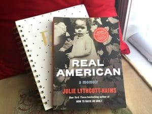 Book "Real American" by Julie Lythcott-Haims rests on a notebook. A young girl is featured on the book cover.