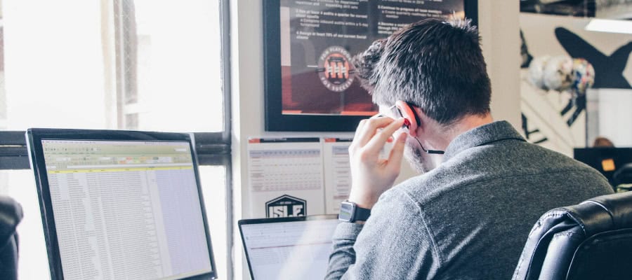 Person working at computer, phone headset on, spreadsheets visible.