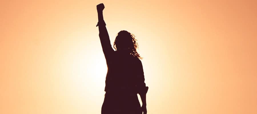 Silhouette of a woman raising a fist in defiance against a sunset.