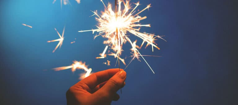 Hand holding a burning sparkler against a dark blue background.
